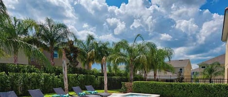 Una piscina con sillones de descanso, palmeras y cielo despejado.