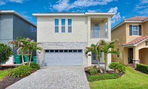 A two-story house with a garage, stone facade, and a well-maintained lawn with palm trees. - 8BR Encore Villa With Galactic Game Room (Kissimmee)