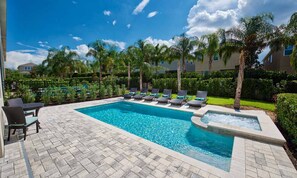 A rectangular swimming pool with a hot tub, surrounded by lounge chairs and a table with chairs. - 8BR Encore Villa With Galactic Game Room (Kissimmee)