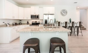 A modern kitchen with white cabinets, a stainless steel refrigerator, a microwave, and a clock on the wall. - 8BR Encore Villa With Galactic Game Room (Kissimmee)