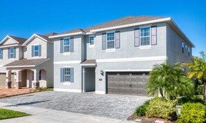 A two-story residential building with a garage, a covered driveway, and a well-maintained lawn with palm trees. - Colorful Villa With Theater at Encore (Kissimmee)