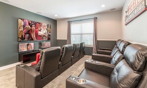 A home theater room with leather recliners, a large flat-screen TV, and a wall-mounted projector screen. - Colorful Villa With Theater at Encore (Kissimmee)