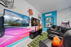 Ein Zimmer mit einem großen Fernseher, einem Basketballkorb, einem Kunstwerk mit Minions, einer Spielkonsole und einem Sofa.