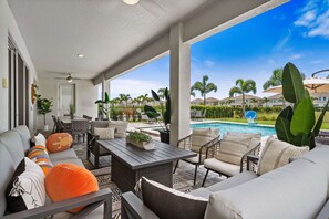 Ein überdachter Außenbereich mit Blick auf den Pool, ausgestattet mit Sofas, Sesseln und einem Tisch.