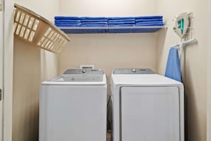 Ein Waschraum mit zwei weißen, frontbeladenen Waschmaschinen und Trocknern, einem blauen Handtuchhalter und einem weißen Bügeleisen auf einem wandmontierten Gestell.