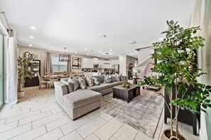A modern living room with a sectional sofa, a dining area, and a kitchen in the background. - Astonishing Villa w/ Home Theater at Encore (Kissimmee)