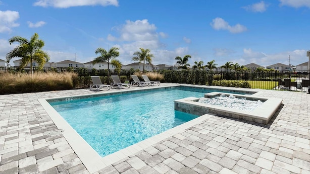 Une piscine rectangulaire avec un jacuzzi, entourée de chaises longues et d’une terrasse en briques.