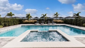 Une piscine rectangulaire avec un jacuzzi au centre, entourée de chaises longues et de palmiers.
