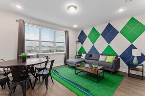 A modern living room with a grey sofa, a round dining table with chairs, and a green artificial turf rug. - 10br Encore Villa, 10 Min From Disney Parks (Kissimmee)