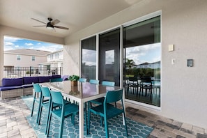 Un patio exterior con puerta de vidrio que da a una zona de piscina, una mesa de comedor con sillas y un sofá.