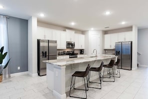 A modern kitchen with white cabinets, stainless steel appliances, and a marble island with bar stools. - 10br Encore Villa, 10 Min From Disney Parks (Kissimmee)