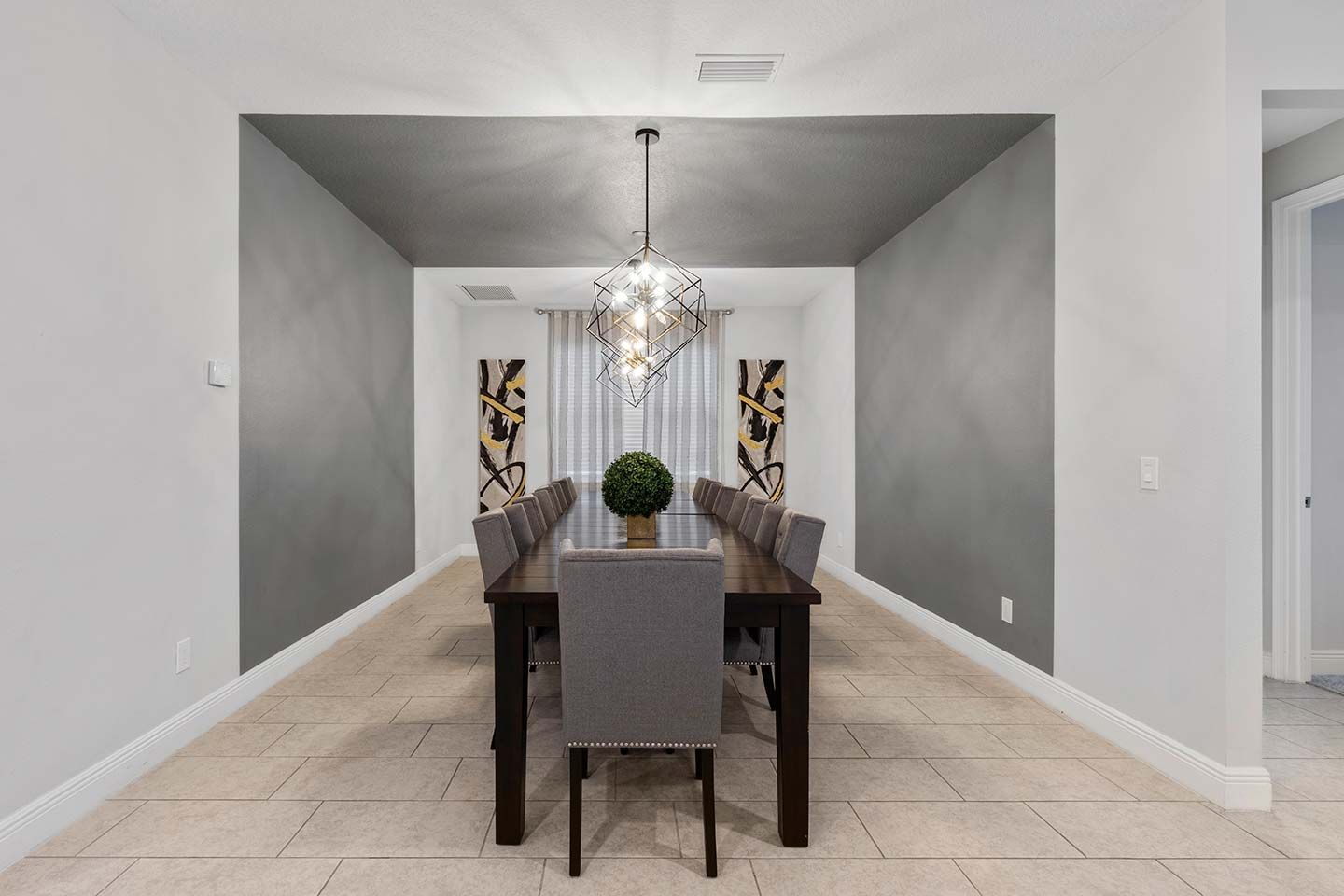 A dining room with a long table, chairs, a chandelier, and abstract wall art.