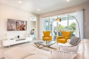 A modern living room with a white sofa, yellow armchairs, a glass coffee table, and a flat-screen TV mounted on the wall. - Encore Estate, 6br, 10 Min to Disney (Kissimmee)