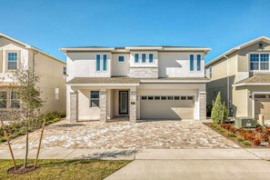 A two-story house with a garage, a covered entryway, and a brick driveway. - Colorful Home With Theater at Encore (Kissimmee)