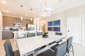 A modern kitchen with stainless steel appliances, a large island with seating, pendant lighting, and artwork on the wall. - Artistic Townhouse With Games Room at Reunion (Kissimmee)