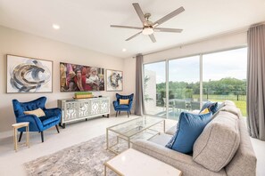 A spacious living room with a large window, a ceiling fan, and a modern fireplace. - Artistic Townhouse With Games Room at Reunion (Kissimmee)