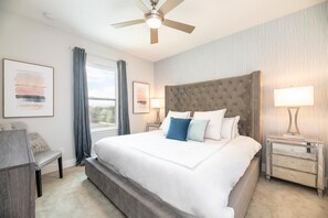 A hotel room with a large bed, a desk, a chair, a ceiling fan, and a window with curtains. - Artistic Townhouse With Games Room at Reunion (Kissimmee)