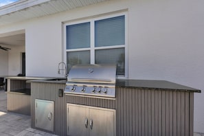 An outdoor kitchen with a grill, sink, and storage cabinets. - Colorful Villa With Game Room in Encore (Kissimmee)