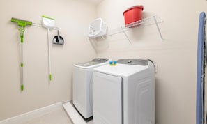 A laundry room with two washing machines, a mop, a broom, a laundry basket, and a red bucket on a shelf. - Captivating Villa With Theater at Encore (Kissimmee)