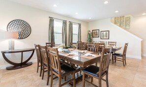 A dining area with a round table, wooden chairs, and a side table with a lamp. - 10br Encore Villa Pool, Spa & TV Loft (Kissimmee)
