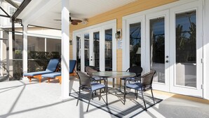 Un patio cubierto con mesa y sillas, una tumbona y un acceso por puerta de vidrio.