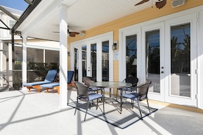 A covered patio with a table and chairs, a sun lounger, and a glass door entrance. - Beaming Home With Private Pool at Reunion (Kissimmee)