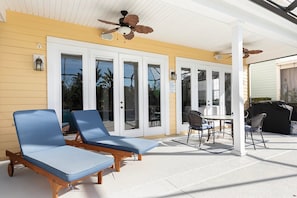 A covered outdoor seating area with two lounge chairs, a table, and chairs, and a ceiling fan. - Beaming Home With Private Pool at Reunion (Kissimmee)
