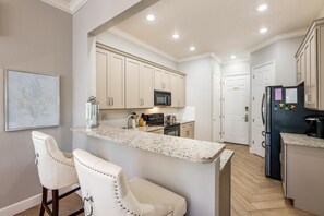 Una cocina con armarios blancos, encimera de granito, refrigerador y microondas.