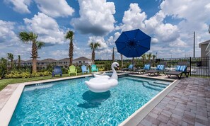 A swimming pool with a swan float, lounge chairs, and a blue umbrella. - Colorful Bright Home With Fun Loft in Encore (Kissimmee)