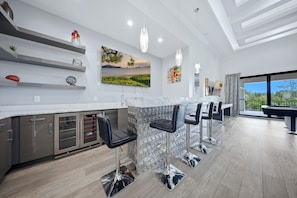 A modern kitchen with a bar area, stainless steel appliances, and a large window offering a view. - Deluxe Mansion With Swim up Bar and Pool Slide at Reunion (Kissimmee)