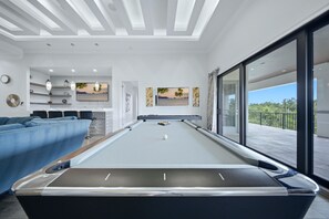 A modern indoor pool area with a pool table, seating, and artwork on the walls. - Deluxe Mansion With Swim up Bar and Pool Slide at Reunion (Kissimmee)