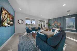 A modern living room with a sofa, coffee table, and a large painting on the wall. - Bohemian Chic Villa With Themed Bedrooms at Reunion (Kissimmee)