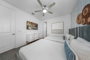 Ein modernes Schlafzimmer mit Deckenventilator, einem Bett mit weißer Bettwäsche, einem Schminktisch und einem Gemälde an der Wand.