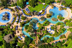 Ein Luftbild eines Resorts mit mehreren Schwimmbecken, Palmen und Liegestühlen.