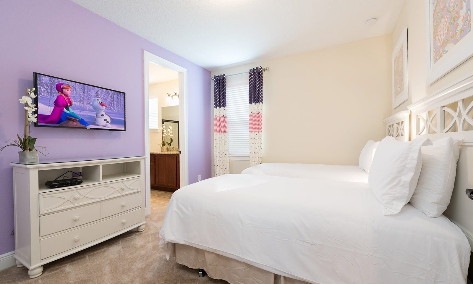 Une chambre à coucher comprenant un lit, une commode, un téléviseur et une porte donnant sur une salle de bain.