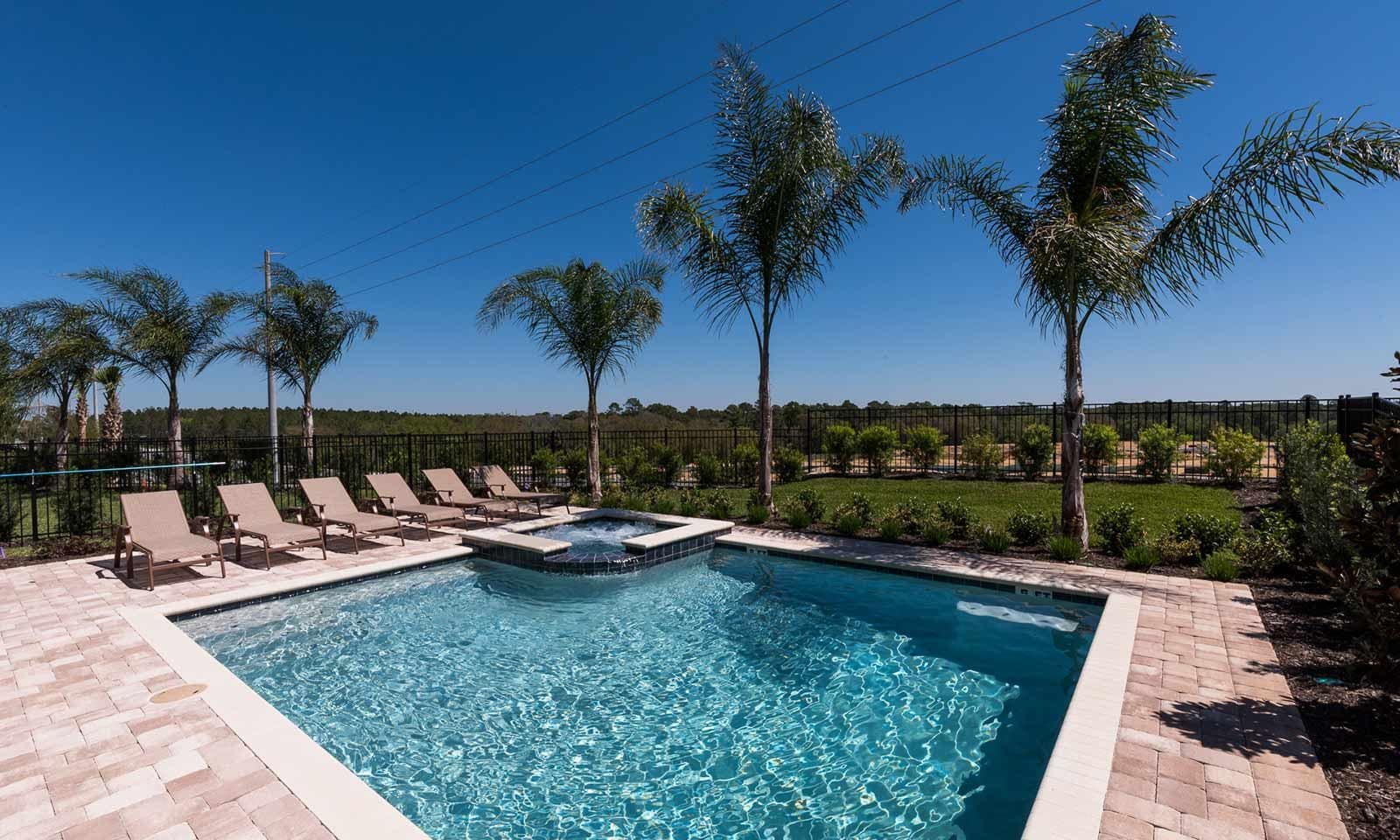 A rectangular swimming pool with a hot tub, surrounded by lounge chairs and palm trees.
