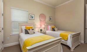 A bedroom with two beds, a window with blinds, a bedside table with a lamp, and a decorative mirror. - Bright Home With Game Room Theater at Reunion (Kissimmee)