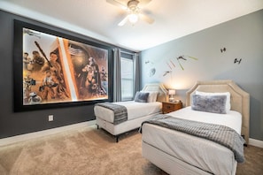 A bedroom with two beds, a ceiling fan, a large framed poster on the wall, and a carpeted floor. - Encore 6BR Home, Pool & Game Room, Near Disney (Kissimmee)