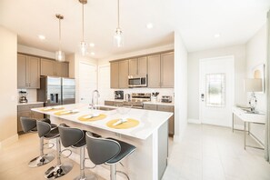 A modern kitchen with a central island, bar stools, stainless steel appliances, and pendant lighting. - Bright and Sunny Townhouse With Games Room at Reunion (Kissimmee)
