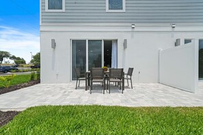 A modern house with a patio area featuring a table and chairs, a covered sliding door, and a well-maintained lawn. - Blue Suede Townhome in Reunion Resort (Kissimmee)