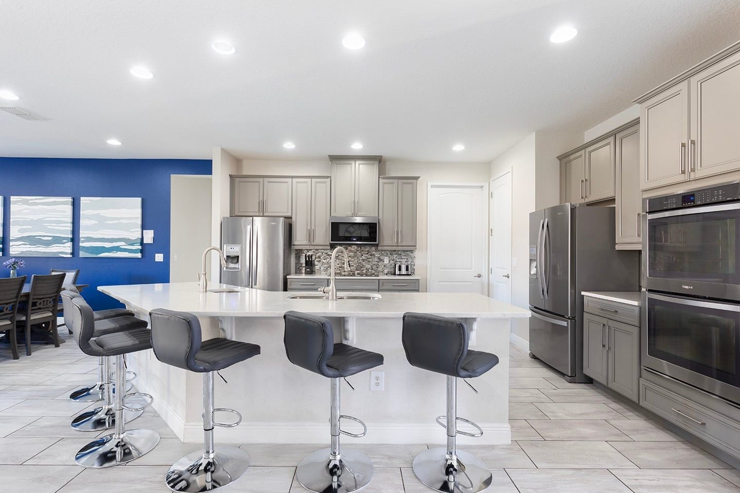 A modern kitchen with stainless steel appliances, a central island with bar stools, and a blue accent wall.