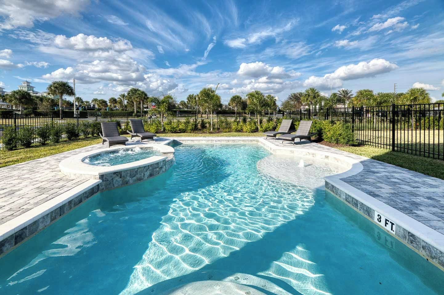 A swimming pool with a hot tub, surrounded by lounge chairs and palm trees.