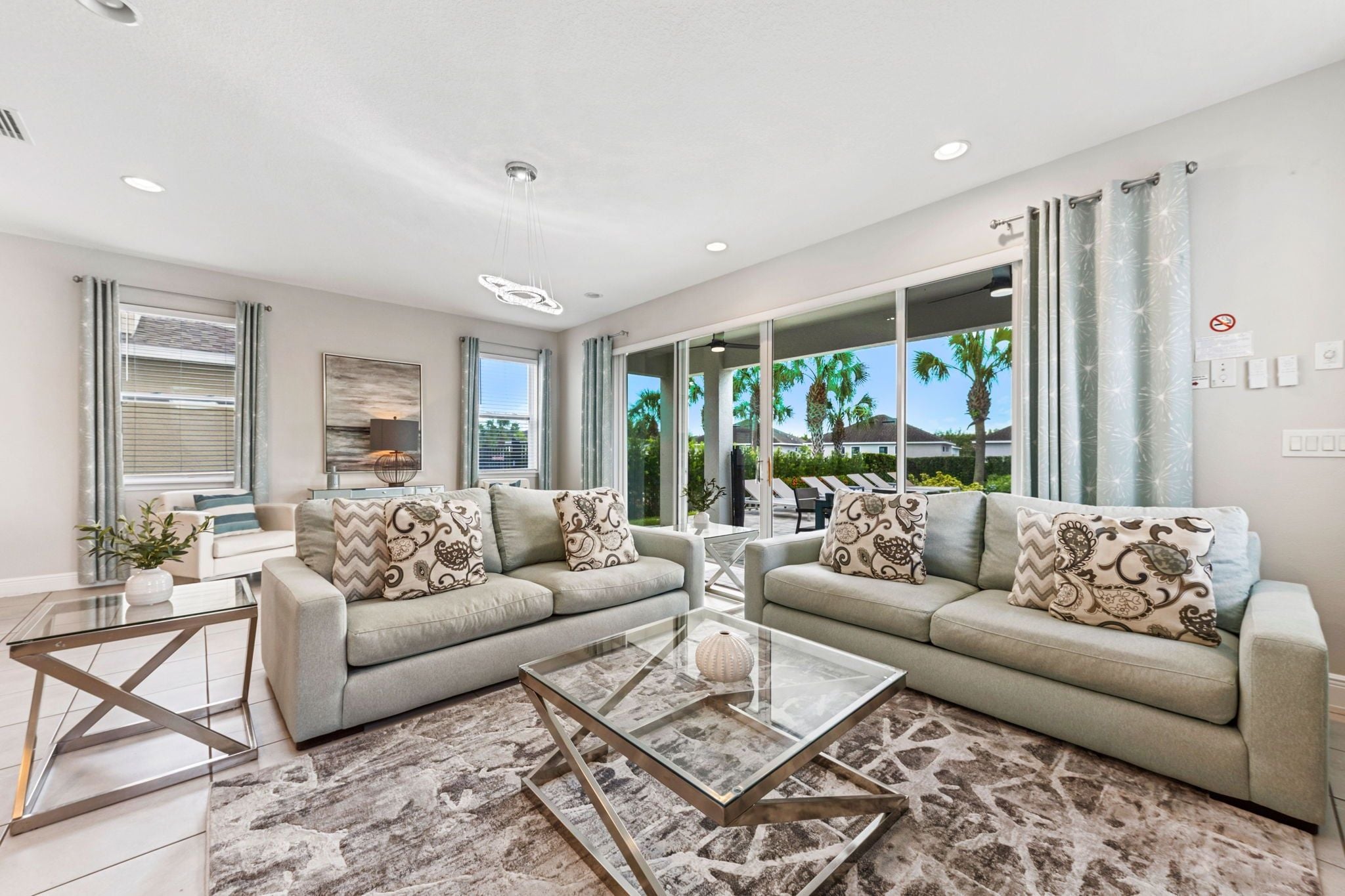 A modern living room with two sofas, a glass coffee table, and a large window with a view of palm trees.