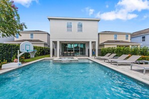 A swimming pool with a basketball hoop, lounge chairs, and a building with large windows. - Airy House With Private Pool in Encore (Kissimmee)