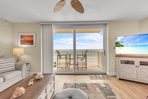 Ein Wohnzimmer mit Blick auf den Strand, inklusive einer Couch, einem Couchtisch mit Dekoration, einem Fernseher und einem Essbereich mit Stühlen.