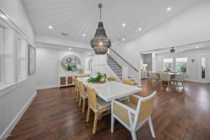 A spacious dining area with a white table and wicker chairs, a staircase, and a large chandelier. - Charming Vacation Retreat just steps from Siesta Key Beach with heated pool. (Siesta Key)