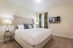 A hotel room with a large bed, two bedside tables, a wall-mounted TV, and a window with curtains. - Encore Villa: 7br, Games, Pool, Near Disney (Kissimmee)