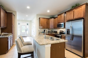 A modern kitchen with granite countertops, stainless steel appliances, and wooden cabinets. - Encore Villa: 7br, Games, Pool, Near Disney (Kissimmee)