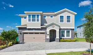 A two-story house with a garage, a front entrance with a decorative arch, and a well-maintained lawn. - Spacious Abode With Spillover Spa in Encore (Kissimmee)
