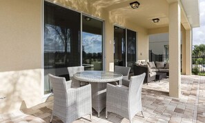 An outdoor patio with a round table and wicker chairs, a sofa, and a glass door leading to a covered area. - Lively Home With Galactic Themed Bedroom at Encore (Kissimmee)